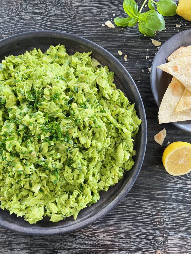 grøn salat med grøn dressing i sort rundt keramikfad på sort træbord med citroner på siden