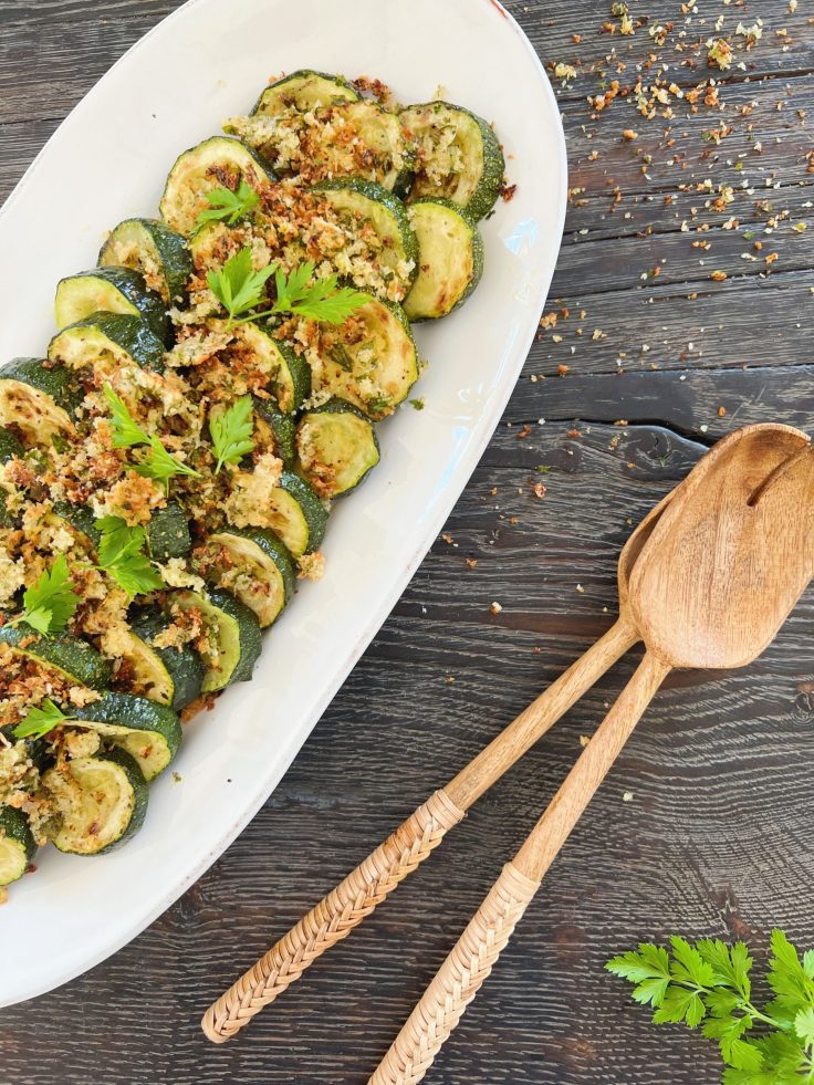 en squashsalat med sprød topping af pankorasp anrettet på et hvidt ovalt serveringsfad i keramik fra casagent. salaten står på et sort rustikt træbord og ved siden af ligger der et brunt salatbestik i mangotræ. Salaten er pyntet med lidt kviste persille